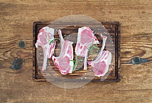 Rack of Lamb with rosemary and spices on rustic chopping board over old wooden background.