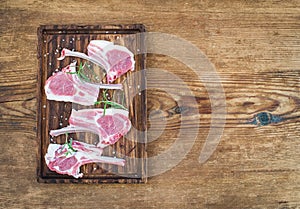 Rack of Lamb with rosemary and spices on rustic chopping board over old wooden background.