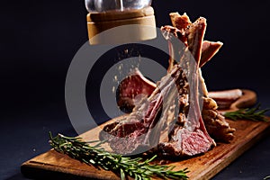 Rack of lamb with rosemary on wooden cutting board over dark background, side view, selective focus