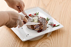 Rack of lamb served with pomegranate seeds and sauce on white plate. Close-up hands cutting rack of lamb meat cutlet.