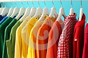 Rack with rainbow clothes on color background