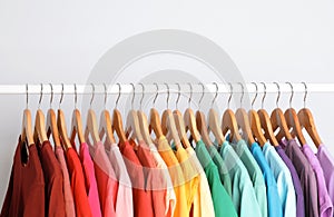 Rack with rainbow clothes on light background