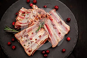 Rack of raw spare pork ribs flavored with spices on a black slate with paprika, bay leaves on the background, top view, close-up