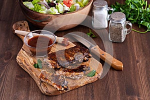 A rack of spareribs covered in barbecue sauce on a wooden board.