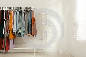 Rack with stylish clothes near white wall indoors. Fast fashion