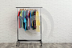 Rack with stylish clothes near white wall. Space for text