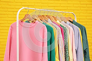 Rack with stylish clothes near yellow brick wall