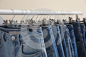 Rack with stylish jeans on beige background, closeup