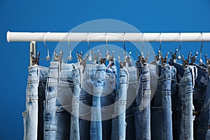 Rack with stylish jeans on blue background