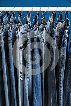 Rack with stylish jeans on blue background, closeup