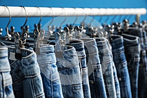 Rack with stylish jeans on blue background, closeup