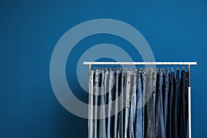 Rack with stylish jeans on blue background. Space for text