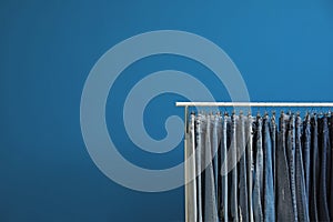 Rack with stylish jeans on blue background. Space for text