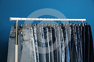 Rack with stylish jeans on blue, closeup
