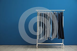 Rack with stylish jeans near blue wall. Space for text