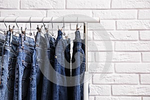 Rack with stylish jeans near brick wall