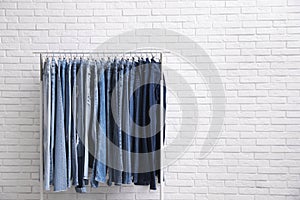 Rack with stylish jeans near brick wall. Space for text