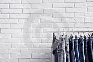 Rack with stylish jeans near brick wall. Space for text