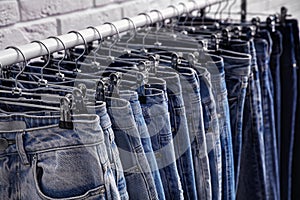 Rack with stylish jeans near wall, closeup