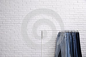 Rack with stylish jeans near wall. Space for text