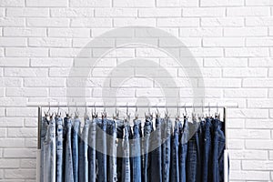 Rack with stylish jeans near wall. Space for text