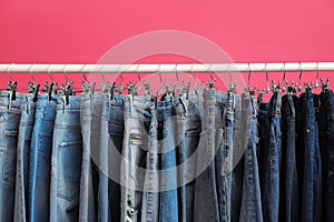 Rack with stylish jeans on pink background