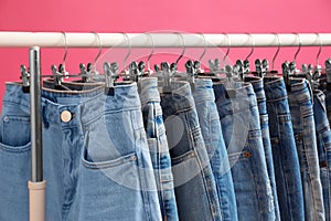 Rack with stylish jeans on pink, closeup