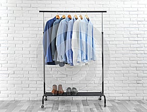 Rack with stylish men`s clothes near brick wall. Space for text