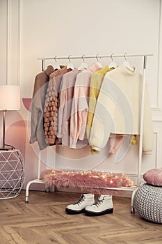 Rack with stylish warm clothes and shoes in modern dressing room