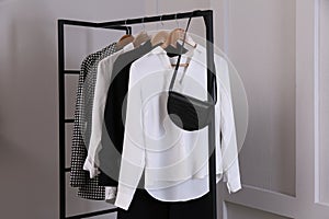 Rack with stylish women`s clothes and bag near light wall
