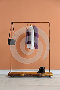 Rack with stylish women`s clothes and boots near wall