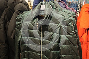 Rack with trendy warm coats of green color in clothes shop