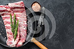 Rack of uncooked raw pork spare ribs seasoned with spices in a pan. Black background. Top view. Copy space