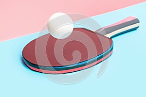 Racket with table tennis ball on blue and pink background close-up.