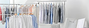 Racks with clean clothes on hangers indoors, banner design. Dry-cleaning service