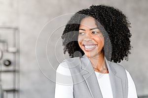 A radiant African-American businesswoman smiles confidently, standing in a modern office environment