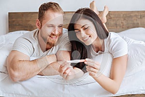Radiant couple looking at pregnancy test in bed