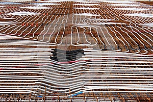 Radiant floor heating system being installed at building construction site with densely laid plastic water pipes on top of rusted