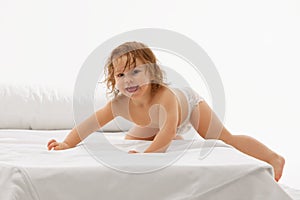 Radiant and playful child, little baby-girl in diaper enjoying fun time on comfortable white bedspread against white