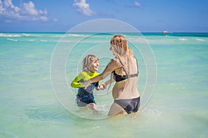 A radiant pregnant mother and her excited son share a tender moment on a serene, snow-white beach, celebrating