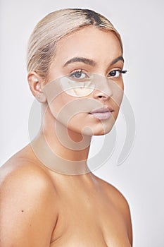 Radiant skin is a game changer. Studio shot of a beautiful young woman wearing an under-eye beauty patch against a grey