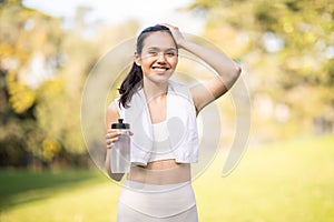 A radiant, smiling woman takes a break from her workout, holding a water bottle