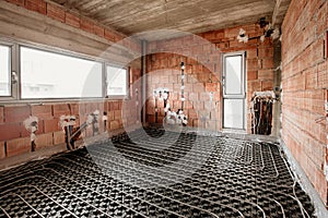 Radiant underfloor heating installation with flexible tubing mounted on construction site. Electrical wires and tubes in building