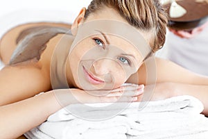 Radiant woman lying on a massage table with mud