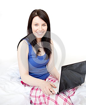 Radiant woman using a laptop sitting on bed