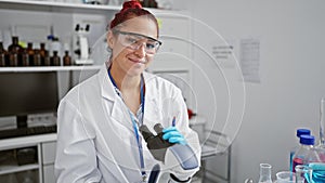 Radiant young redhead woman scientist smiling while performing biolological analysis with microscope in the heart of a high-tech