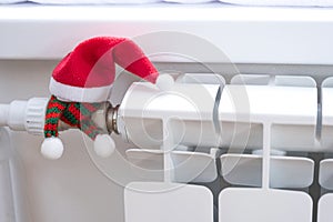 Radiator in the house is wrapped in a knitted scarf and a hat. Warmth and comfort in the house, insulation, winterization. Festive