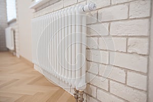 Radiator and thermostat in the apartment - heater close-up. Apartment interior - radiator on a white brick wall