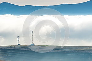 Radio antennas in front of dense fog, blue mountains