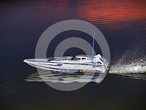 Radio controlled boat at sunset speeding on the water